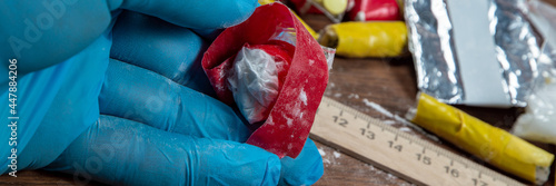 evidence of smuggling traffic: Packaging of a narcotic substance in the hand of a forensic expert against the background of other arrested materials, cocaine, heroin, spice