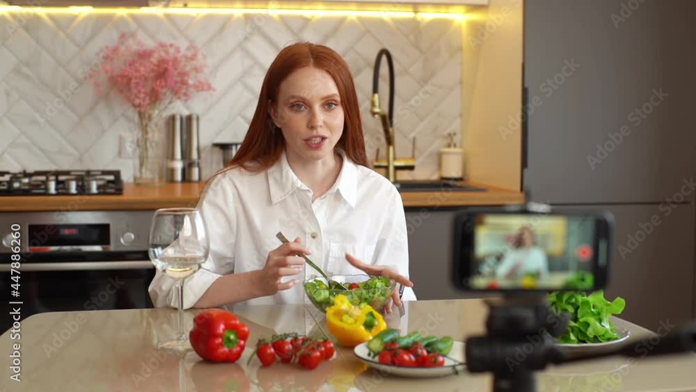Cheerful female vlogger recording live tutorial video about healthy vegetarian eating to followers. Portrait of happy young woman blogger shooting culinary show speaking about salad at home in kitchen Cheerful female vlogger recording live tutorial video about healthy vegetarian eating to followers. Portrait of happy young woman blogger shooting culinary show speaking about salad at home in kitchen