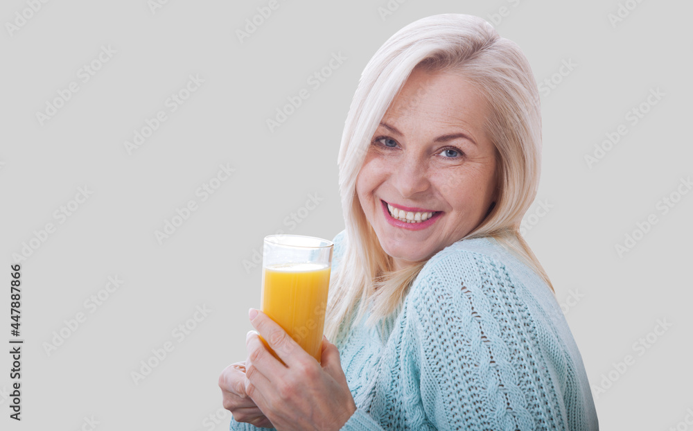 Happy woman holds a glass of orange juice and looks relaxed at the camera isolated on grey. Happy woman holds a glass of orange juice and looks relaxed at the camera isolated on grey.