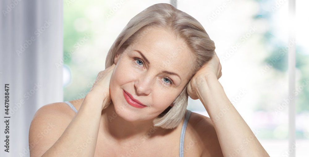 Happy beautiful middle-aged blonde woman shows off her perfectly well-groomed face and sitting relaxed near the window. Realistic images. Happy beautiful middle-aged blonde woman shows off her perfectly well-groomed face and sitting relaxed near the window. Realistic images.