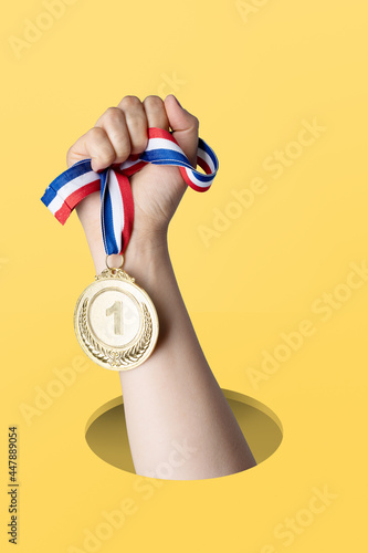 Hand of woman holding gold medal on yellow background.award and victory concept.copy space