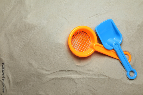 Fotografie Plastic toy shovel and sieve on sand, flat lay