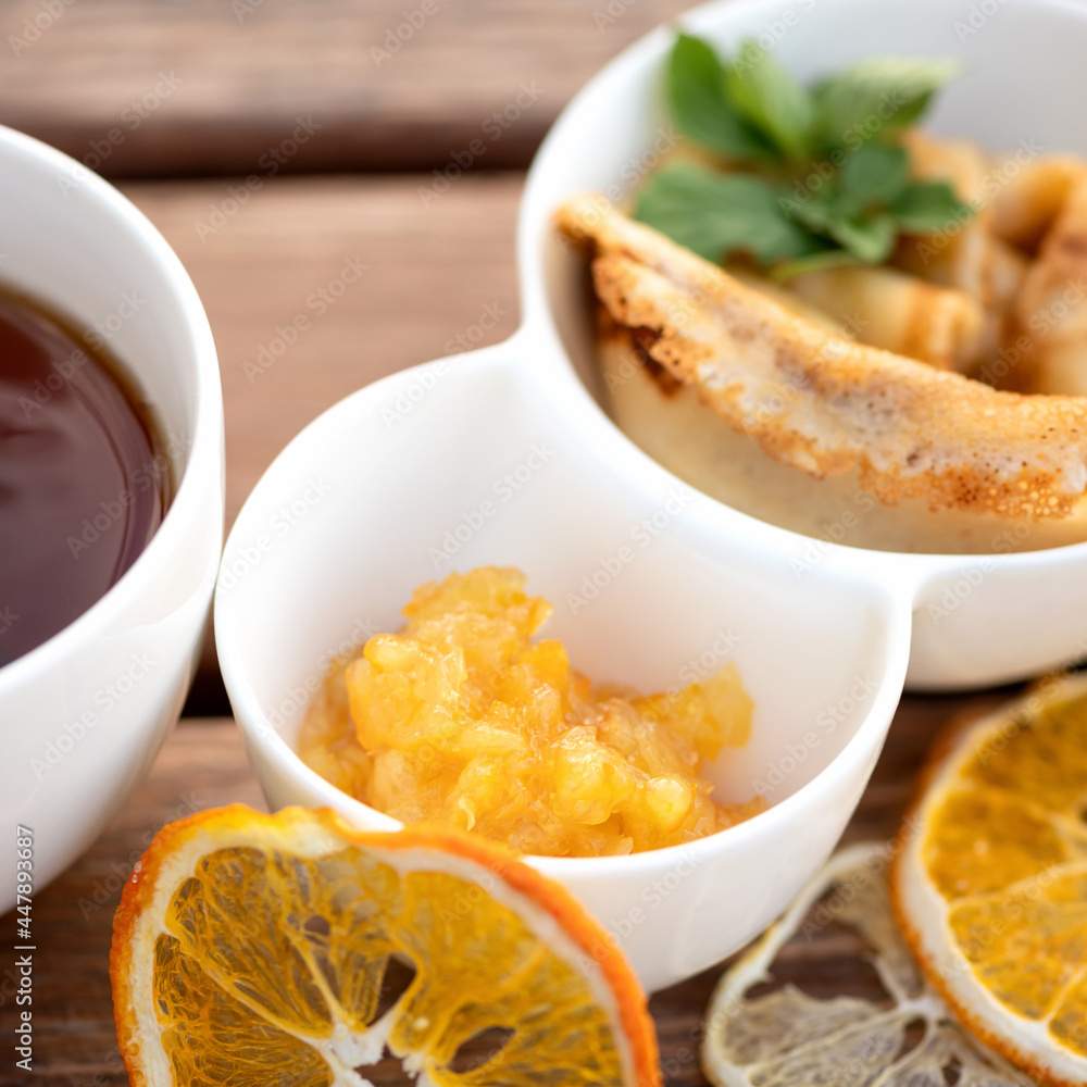 Orange jam with simple pancakes or crepes and cup of tea on rustic table. Delicious American breakfast or dessert. Soft focus. Orange jam with simple pancakes or crepes and cup of tea on rustic table. Delicious American breakfast or dessert. Soft focus.