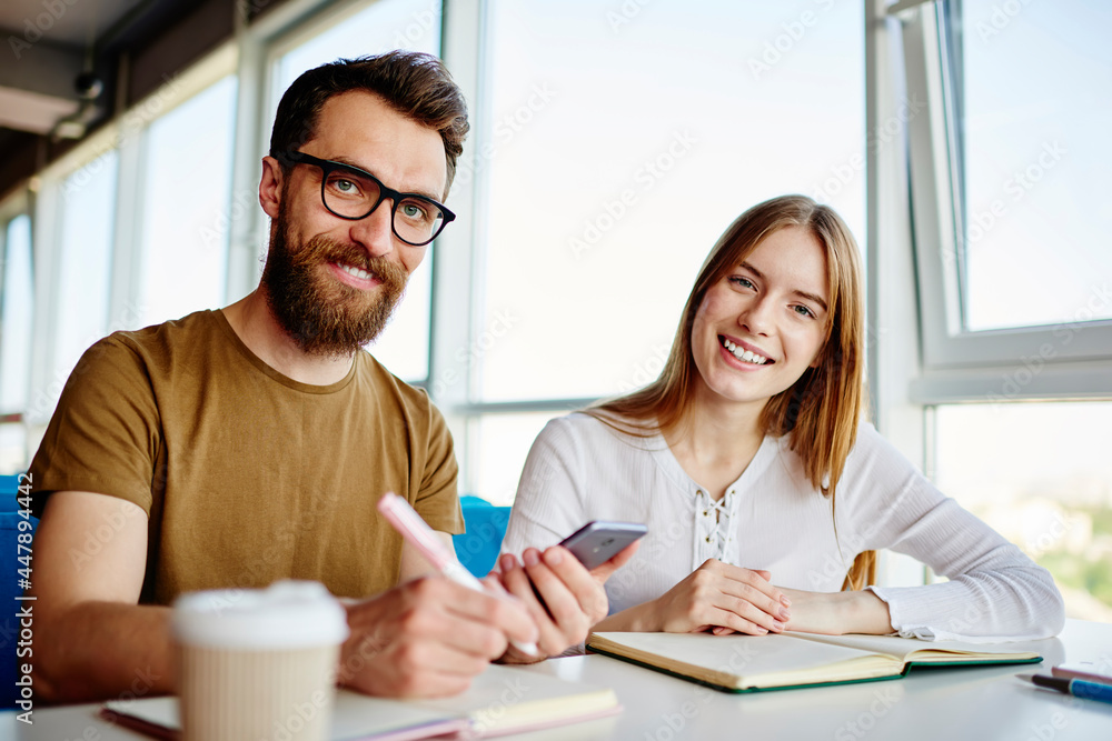 Portrait of cheerful male and female students smiling at camera during together learning in campus, happy Caucasian bloggers posing during daytime meeting for discussing mobile phoning via app Portrait of cheerful male and female students smiling at camera during together learning in campus, happy Caucasian bloggers posing during daytime meeting for discussing mobile phoning via app