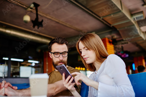 Millennial male and female users browsing web content via cellphone device connecting to 4g internet indoors, young friends discussing received email message while chatting in social networks