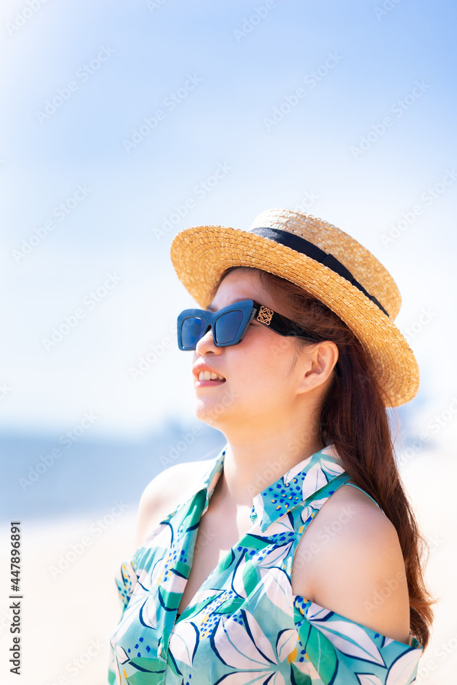 Vertical image. Beautiful Asian women with sea and sky in summer time. Woman wear sunglasses and straw hat. Portrait happy girl. Fashion with travel.