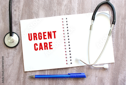White notebook with red text URGENT CARE and a stethoscope on a gray wooden table.