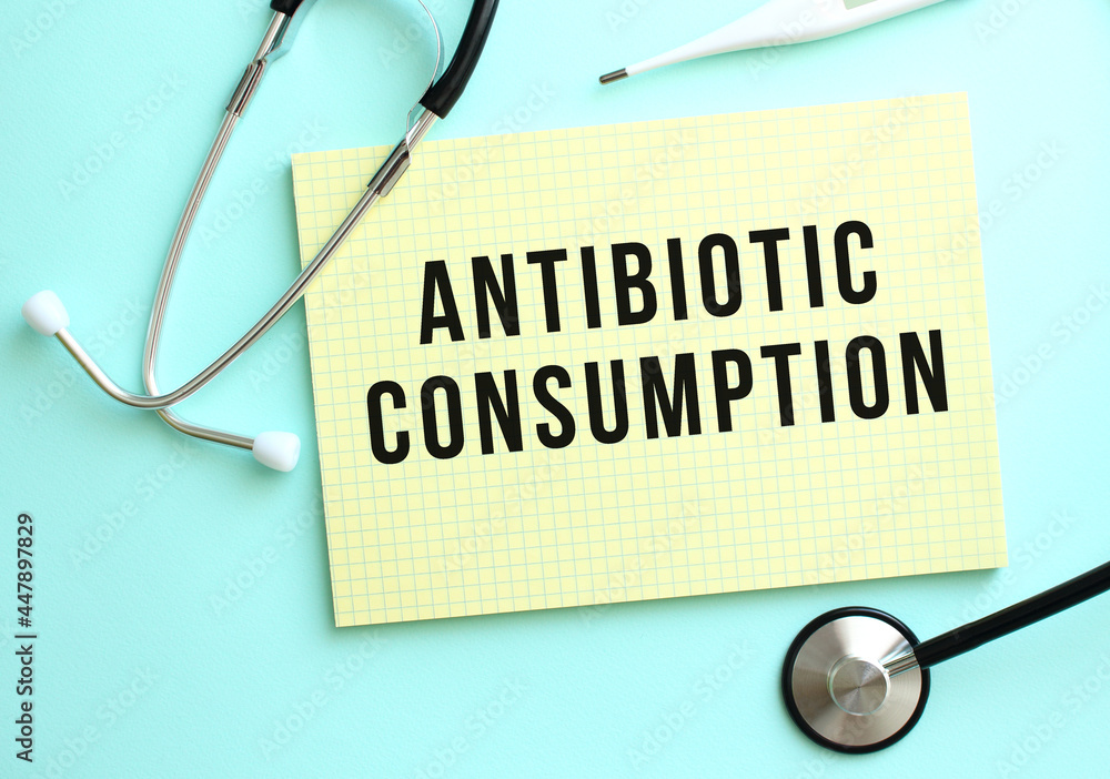 The text ANTIBIOTIC CONSUMPTION is written in a yellow pad that lies next to the stethoscope on a blue background. The text ANTIBIOTIC CONSUMPTION is written in a yellow pad that lies next to the stethoscope on a blue background.