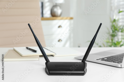 Modern wi-fi router and laptop on white table indoors
