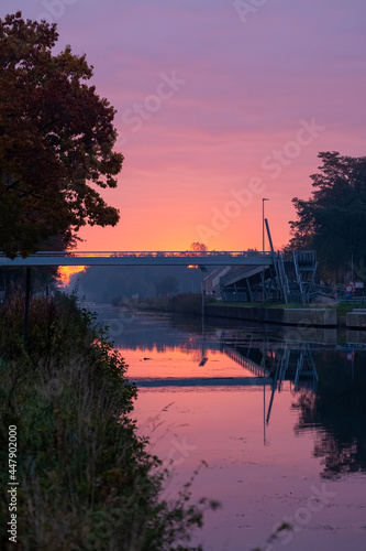 River stream canal and a bridge with grass banks and wild flowers and trees in a scenic landscape on a misty autumns morning sunrise day. High quality photo