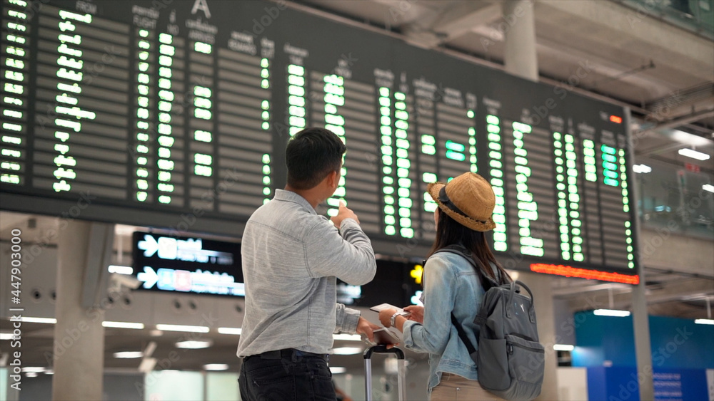 Couple traveler checking flight schedule board in airport terminal