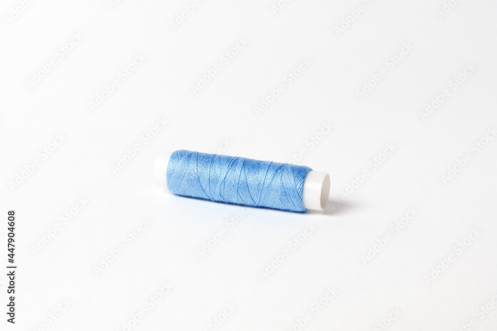 A small bobbin with blue threads on a white background A small bobbin with blue threads on a white background