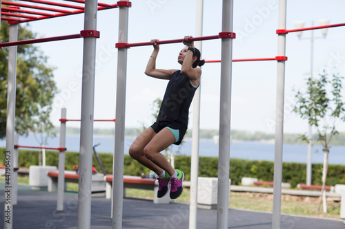 young woman in sport clothes exercising on pull-up bar outdoors sports ground. Healthy lifestyle