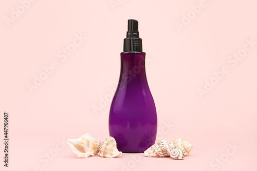 Unbranded purple plastic spray bottle and many different sea shells on pink background. Cosmetic packaging mockup with copy space. Minimalism. Front view