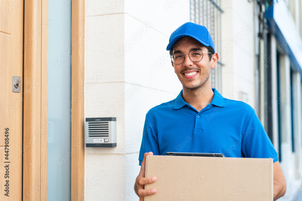 Young delivery man at outdoors holding boxes and a tablet with happy expression Young delivery man at outdoors holding boxes and a tablet with happy expression
