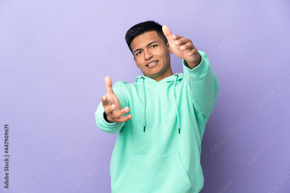 Young Ecuadorian man isolated on purple background presenting and inviting to come with hand Young Ecuadorian man isolated on purple background presenting and inviting to come with hand