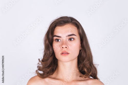 Young beautiful natural soft clean skin woman with freckles light makeup on white background with bare shoulders
