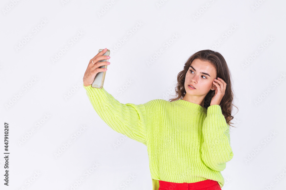 Young beautiful woman with freckles light makeup in sweater on white background with mobile phone take photo selfie Young beautiful woman with freckles light makeup in sweater on white background with mobile phone take photo selfie