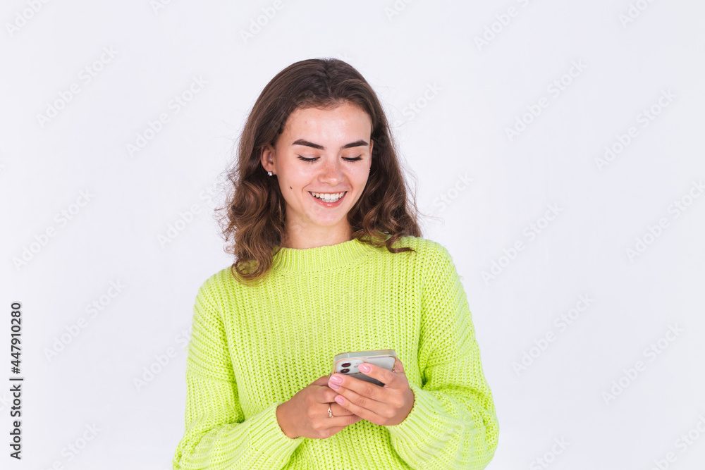 Young beautiful woman with freckles light makeup in sweater on white background with mobile phone texting smile happy Young beautiful woman with freckles light makeup in sweater on white background with mobile phone texting smile happy