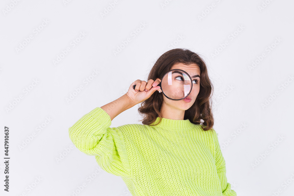 Young beautiful woman with freckles light makeup in sweater on white background with magnifier playful
