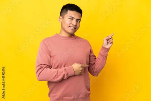 Young Ecuadorian man isolated on yellow background pointing finger to the side