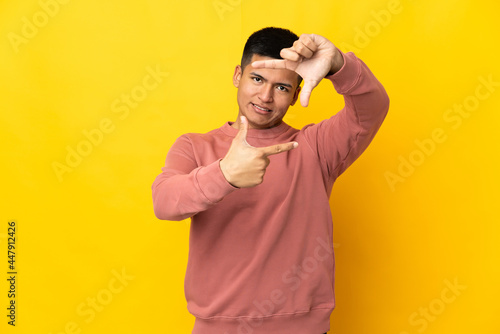Young Ecuadorian man isolated on yellow background focusing face. Framing symbol