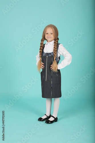 a beautiful little smiling blonde girl in a white shirt and a gray sundress is a schoolgirl