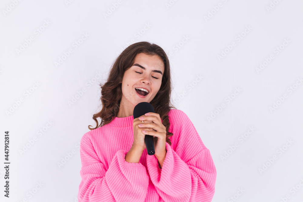 Young beautiful woman with freckles light makeup in sweater on white background with microphone singing favorite song enjoying Young beautiful woman with freckles light makeup in sweater on white background with microphone singing favorite song enjoying