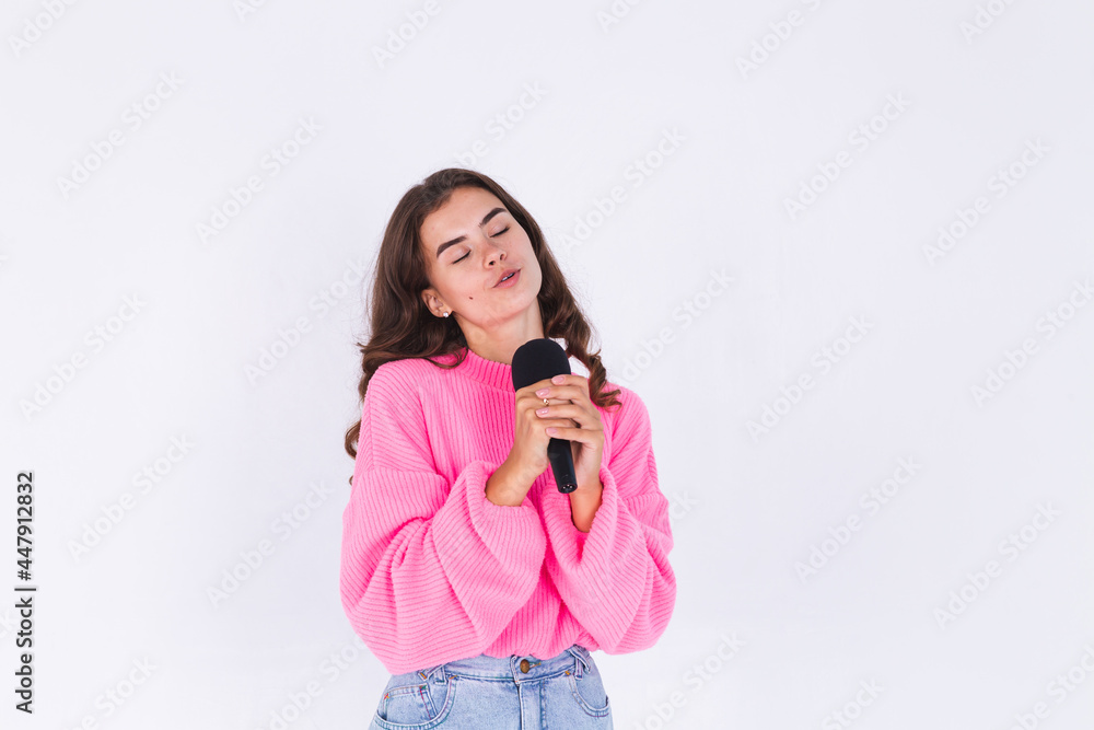 Young beautiful woman with freckles light makeup in sweater on white background with microphone singing favorite song enjoying Young beautiful woman with freckles light makeup in sweater on white background with microphone singing favorite song enjoying