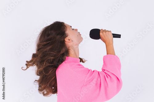Young beautiful woman with freckles light makeup in sweater on white background with microphone singing favorite song enjoying