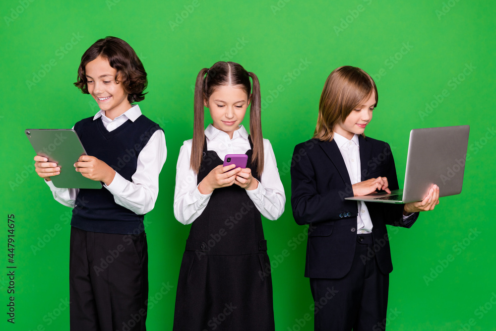 Portrait of three trendy friends friendship addicted kids using devices isolated over bright green color background Portrait of three trendy friends friendship addicted kids using devices isolated over bright green color background