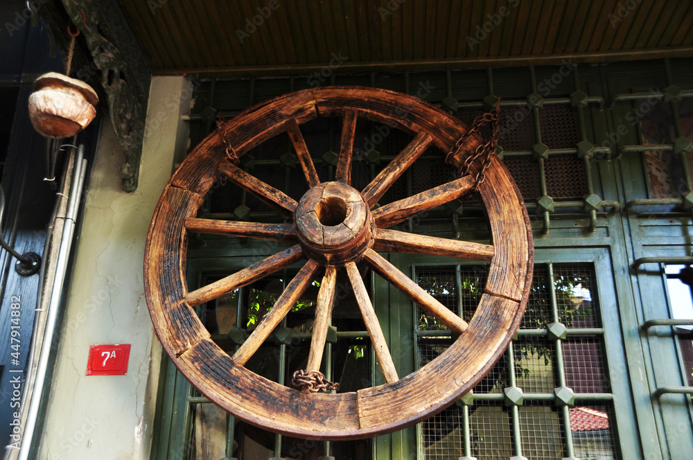 A large wooden wheel from a cart on the window. Decorative element on a window with a metal grill.