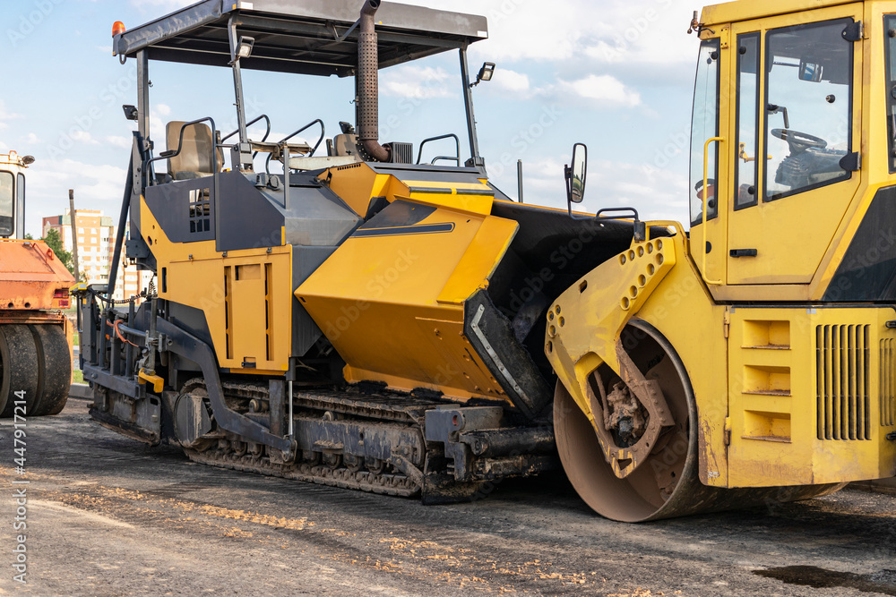 Asphalt paving equipment. Asphalt paver and heavy vibratory roller. Construction of new roads and road junctions. Heavy construction industrial machinery. Asphalt paving equipment. Asphalt paver and heavy vibratory roller. Construction of new roads and road junctions. Heavy construction industrial machinery.
