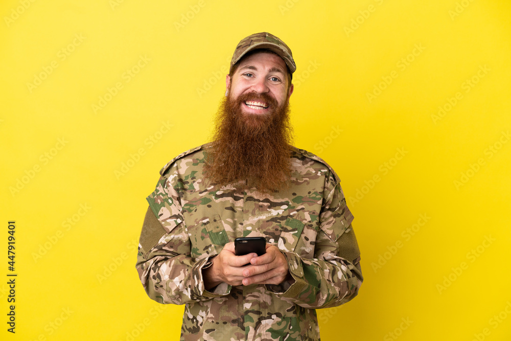 Military Redhead man over isolated on yellow background sending a message with the mobile Military Redhead man over isolated on yellow background sending a message with the mobile