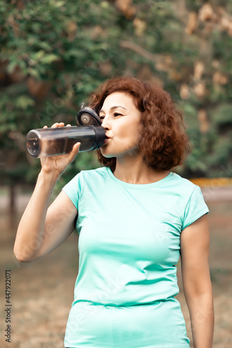 Middle age senior runner woman drinking bottled water after fitness exercise outdoors