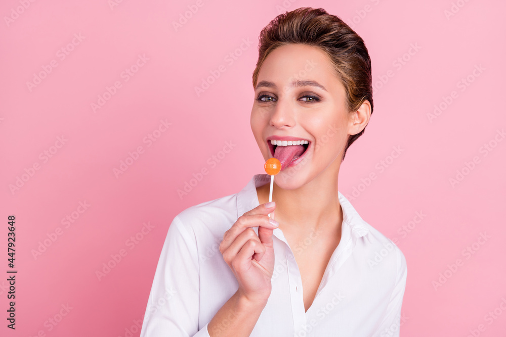 Photo of young happy cheerful positive woman lick tongue llollipop candy isolated on pastel pink color background Photo of young happy cheerful positive woman lick tongue llollipop candy isolated on pastel pink color background