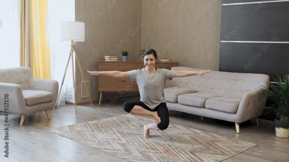 A Young Woman Does Yoga, Does An Exercise For Balance, Sits in The Lotus Position, Is Dressed In Sports Clothes, Is In A Bright Room At Home A Young Woman Does Yoga, Does An Exercise For Balance, Sits in The Lotus Position, Is Dressed In Sports Clothes, Is In A Bright Room At Home