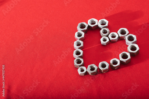 Heart made of steel nuts on red background, concept of love, peace and kindness, leaving space for advertising text