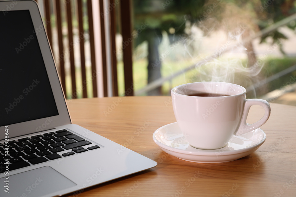 Cup of delicious morning coffee near laptop on wooden table Cup of delicious morning coffee near laptop on wooden table