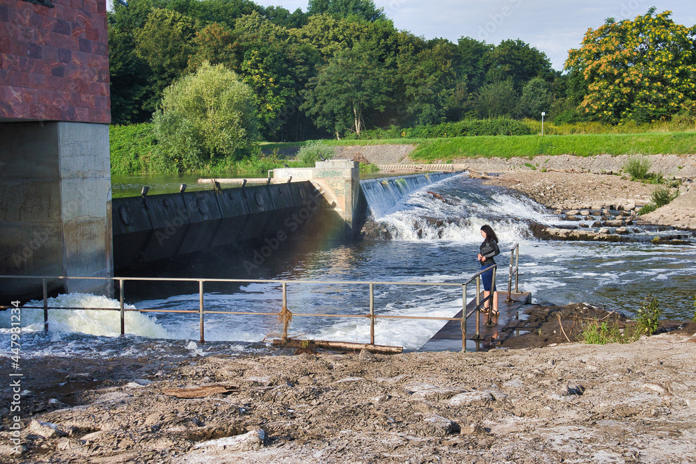 Obraz premium Fließendes Wasser am Luppewehr im Rosental mit Spaziergängerin, Wasserbauwerk an der Neuen Luppe, Leipzig, Kreisfreie Stadt Leipzig, Sachsen, Deutschland