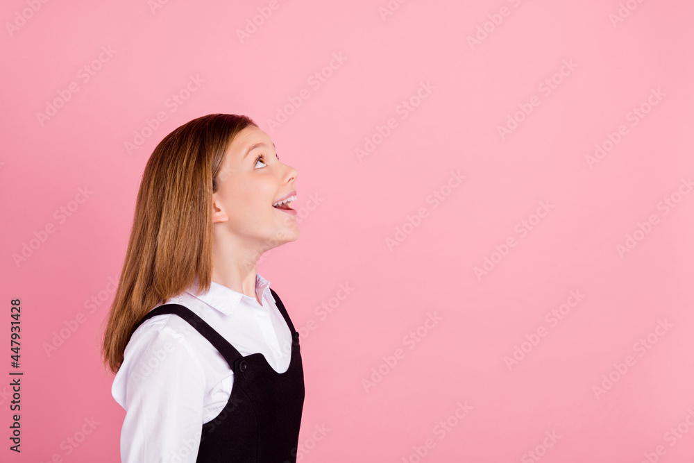 Photo of funny impressed school girl wear white black uniform smiling looking up empty space isolated pink color background