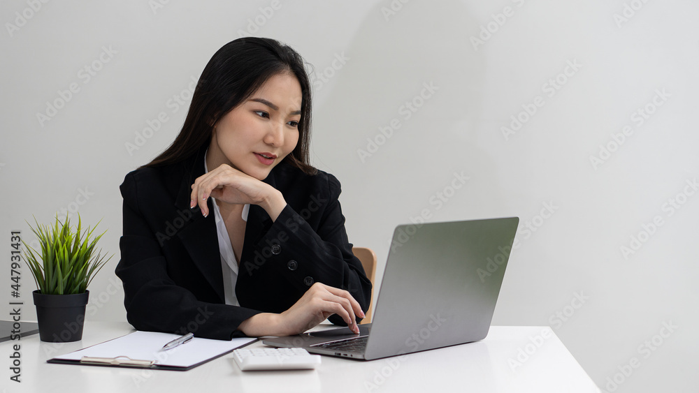 Beautiful Asian businesswoman in a black suit working on a computer at her desk. Small business owners, employees, freelancers, online, SME, marketing, e-commerce Beautiful Asian businesswoman in a black suit working on a computer at her desk. Small business owners, employees, freelancers, online, SME, marketing, e-commerce