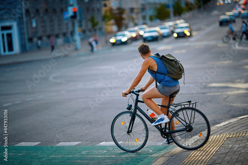 Man rides bike path through pedestrian crossing in evening. Cyclist in city traffic ride on bicycle lane. Man cycling , city traffic on background
