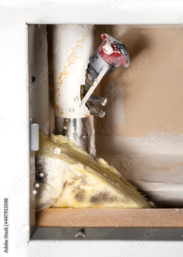 Dripping water from a pipe next to a water shut-off valve from a ceiling hatch in building corridor. Active leak. Cause is a pinhole leak in copper pipe. Selective focus with defocused water droplets.