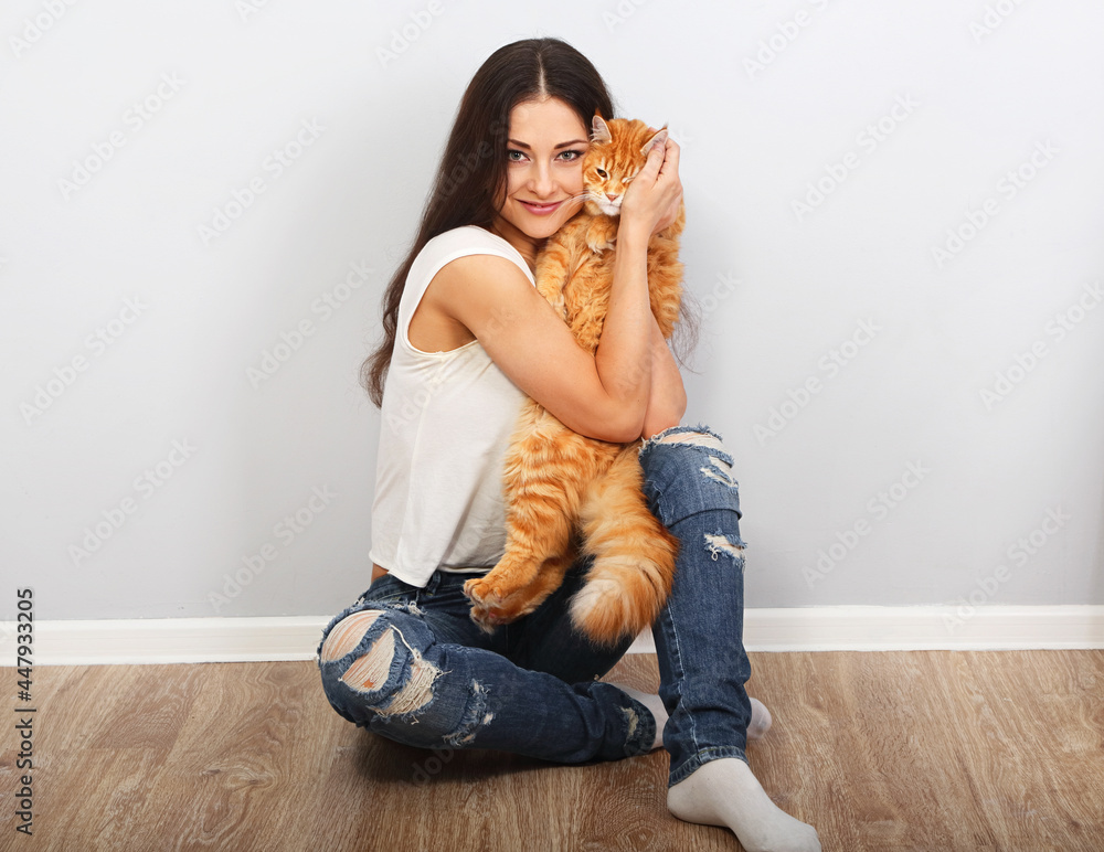 Happy young woman holding and hugging with love on the hands her red maine coon kitten sitting on the floor at home. Closeup Happy young woman holding and hugging with love on the hands her red maine coon kitten sitting on the floor at home. Closeup