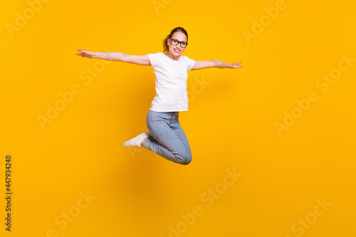 Full size profile side photo of young cheerful woman happy positive smile jump up hands wings isolated over yellow color background © deagreez