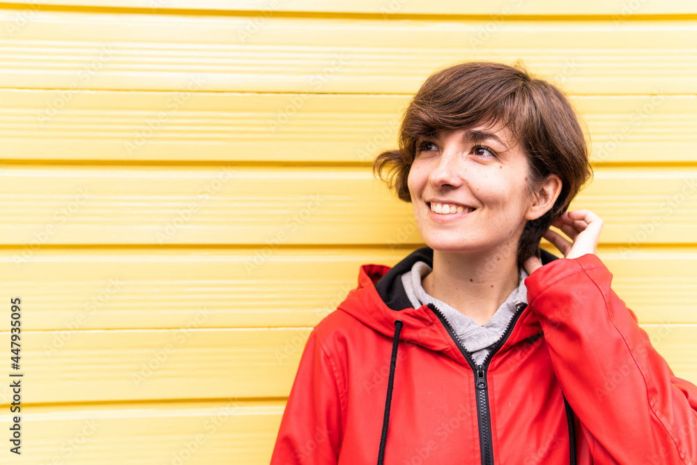 Photo of a young girl with a red raincoat smiling with a yellow background behind her.