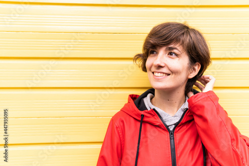 Obraz na płótnie Photo of a young girl with a red raincoat smiling with a yellow background behind her. w salonie