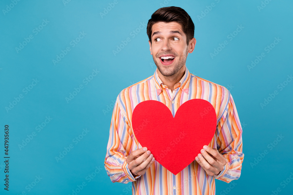 Photo of positive young happy man look empty space amazed hold heart smile isolated on blue color background Photo of positive young happy man look empty space amazed hold heart smile isolated on blue color background