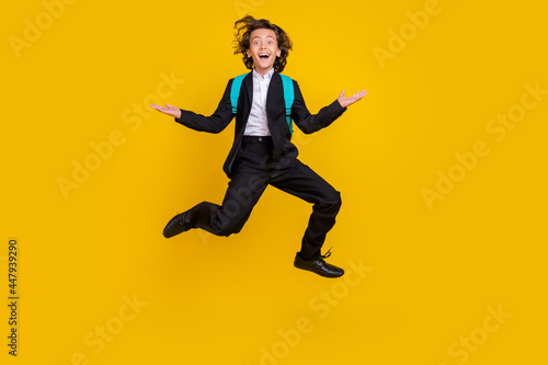 Photo of sporty energetic small boy jump excited mood wear bag black uniform isolated yellow color background